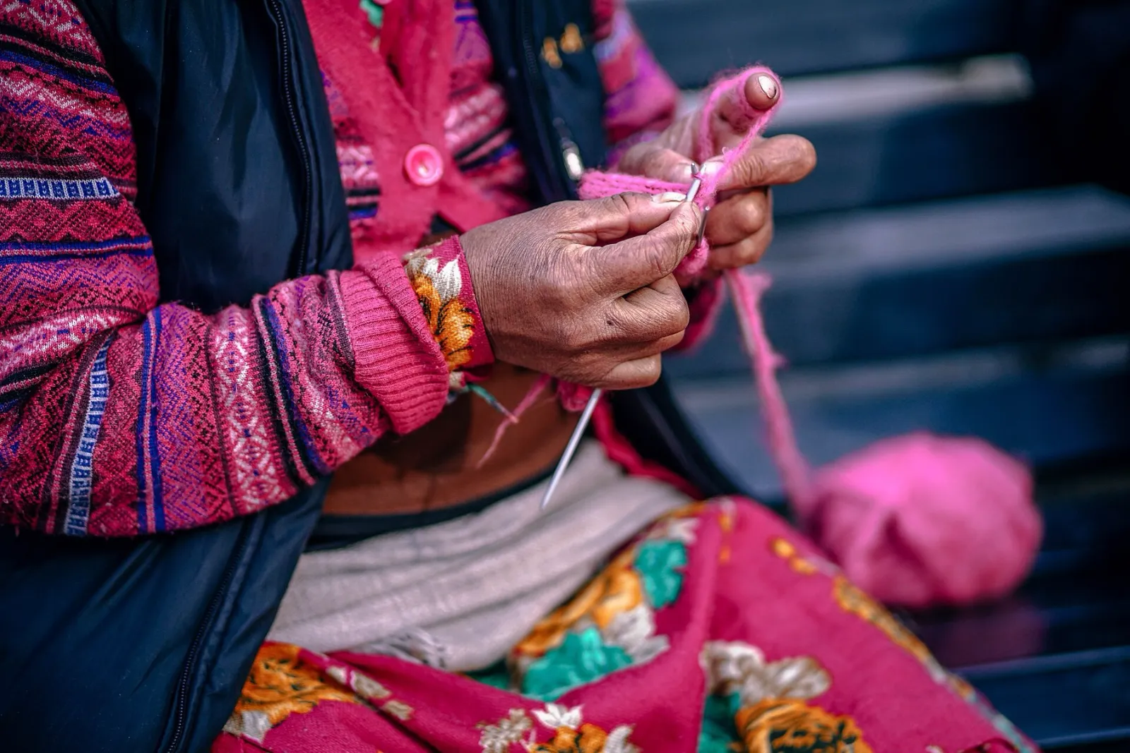 Mãos tricotando um fio rosa com agulhas